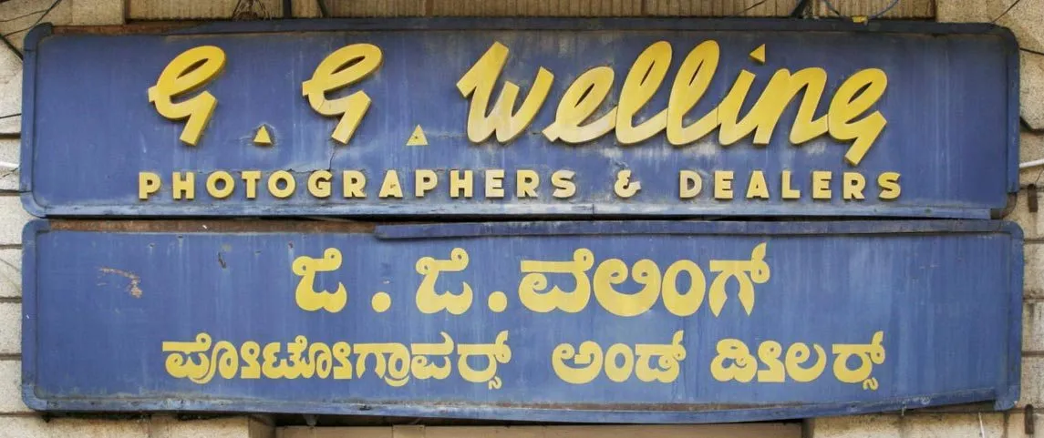 Bilingual sign with wooden English lettering and handpainted Kannada lettering in Bangalore.